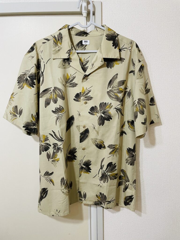 ハンガーに掛けられたユニクロのオープンカラーシャツ。ベージュ地に黒と黄色の花柄が入った夏らしいデザイン。