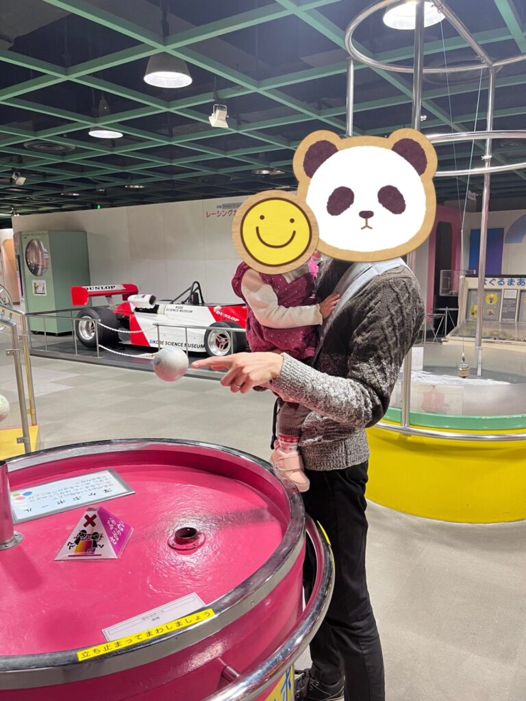展示施設で、大人に抱っこされた子どもが装置を見ている