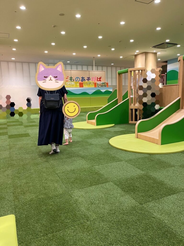 室内の遊び場で、子どもがおばあちゃんと手をつないで滑り台の前を歩いている様子