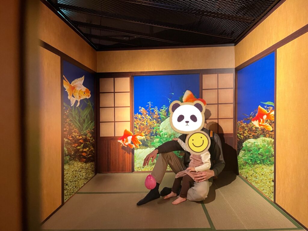 金魚ミュージアムの和室風の展示で、父親が娘を抱っこして座っている様子