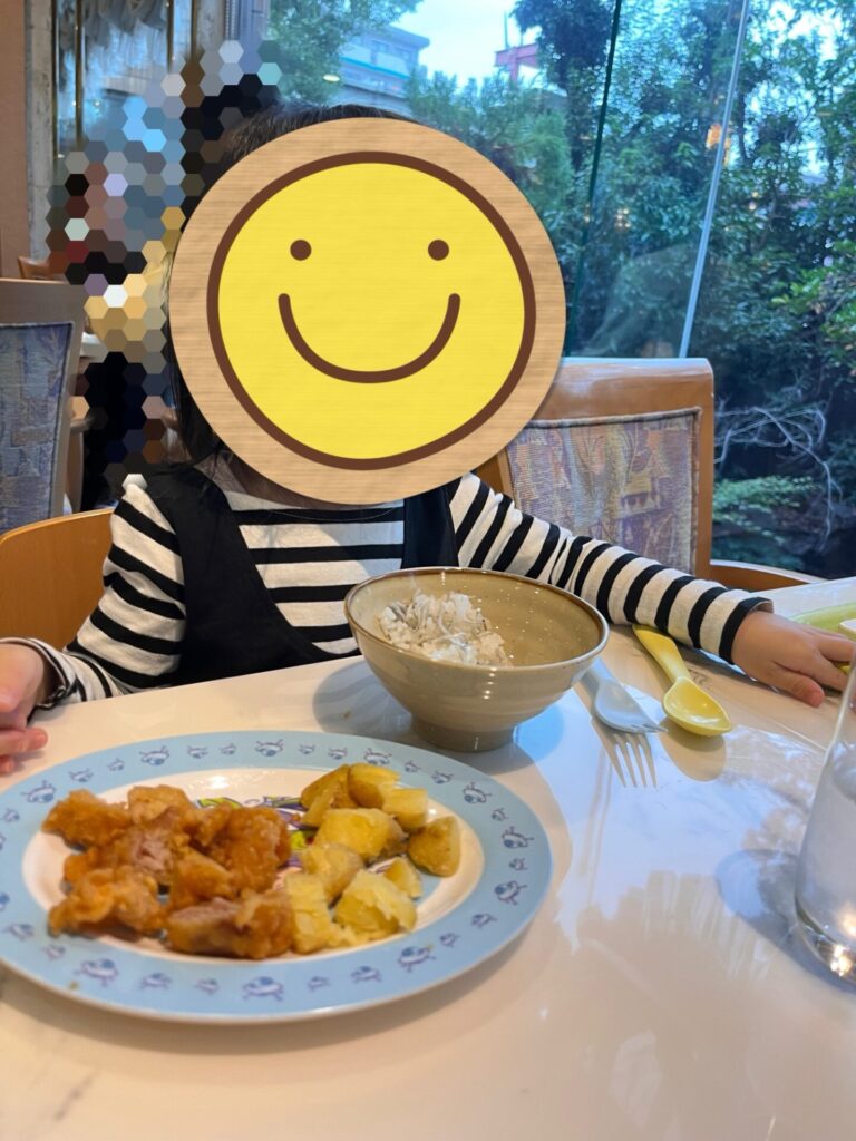 ホテルのバイキング会場で、娘が唐揚げやポテト、ご飯を前に食事している様子