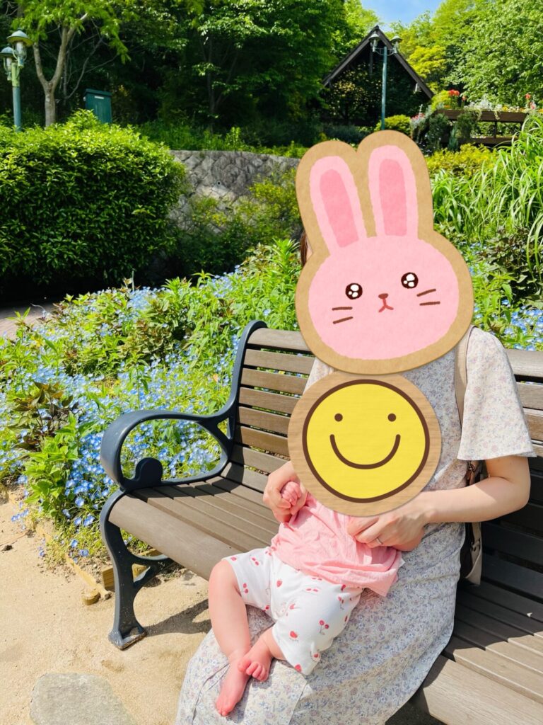 ベンチに座って子どもを抱っこする女性、背景には季節の花が咲くガーデン
