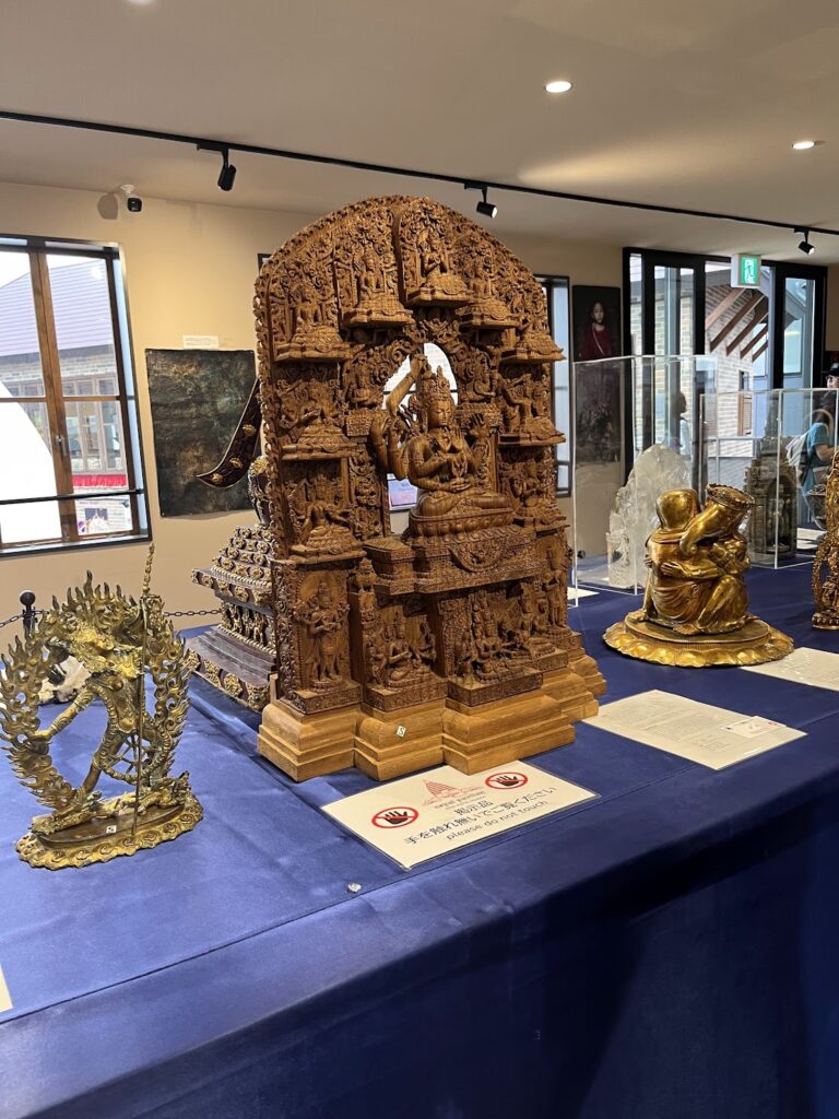 ネパール館の展示品、精巧な木彫りの仏教美術と金属工芸品が並んでいる様子