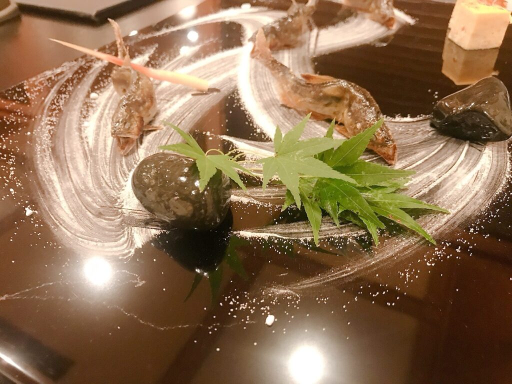 琵琶湖緑水亭で提供された鮎料理の前菜。黒塗りの皿に盛り付けられた鮎と紅葉の葉が美しい。