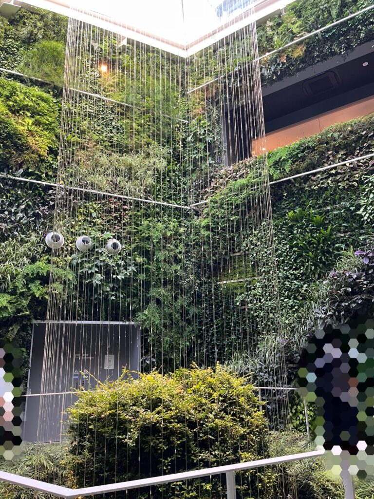 緑の植物に覆われた壁面と天井からの雨のような糸の演出が美しいパビリオン内の写真