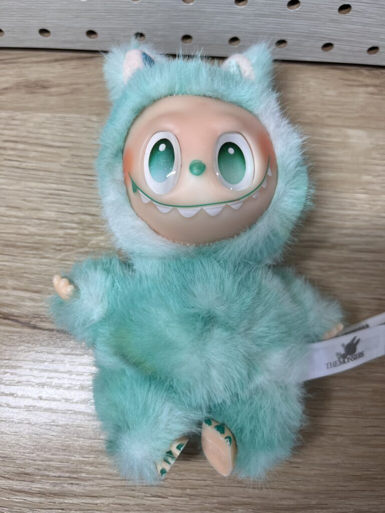緑色のふわふわした体に大きな目とギザギザの歯が特徴的なキャラクター、ラブブのぬいぐるみ。中国のPOP MART「THE MONSTERS」シリーズの一体。