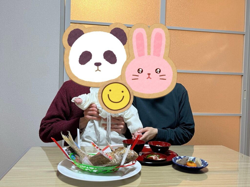 おうちでお食い初め膳を囲み、赤ちゃんを中心に家族で記念撮影している様子。