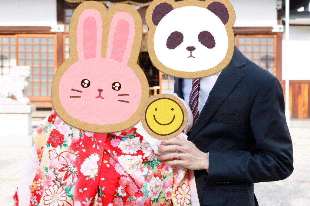お宮参りで赤い祝い着をまとった赤ちゃんを両親が抱いている様子。