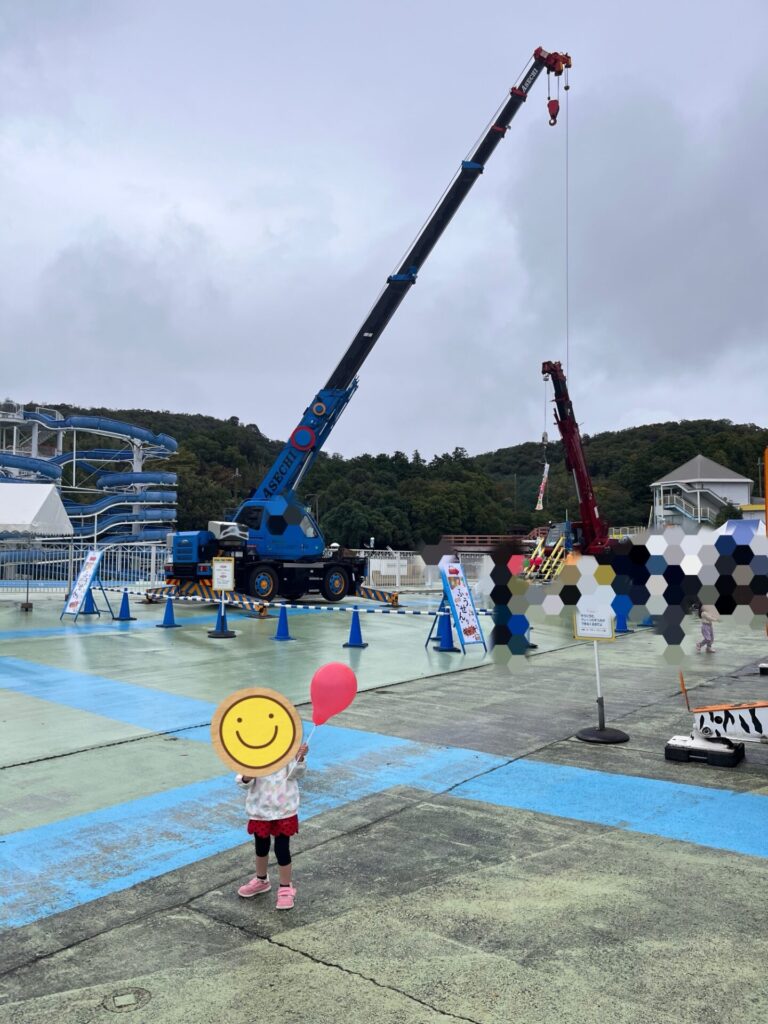 東条湖おもちゃ王国「はたらくくるま大集合」で、クレーン車の前で風船を持って立つ娘。