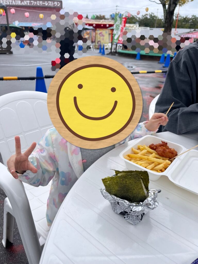 東条湖おもちゃ王国のイベント会場で、屋外テーブルで軽食を楽しむ娘と家族のようす。