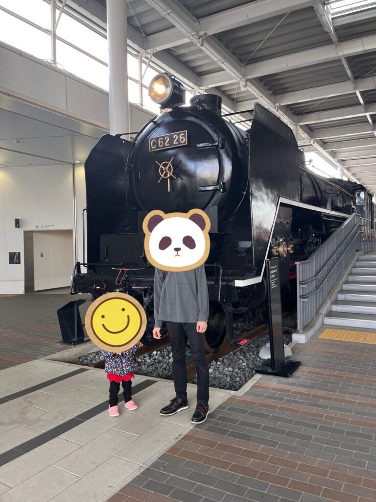 黒いC62形蒸気機関車の前で家族が記念撮影している様子。