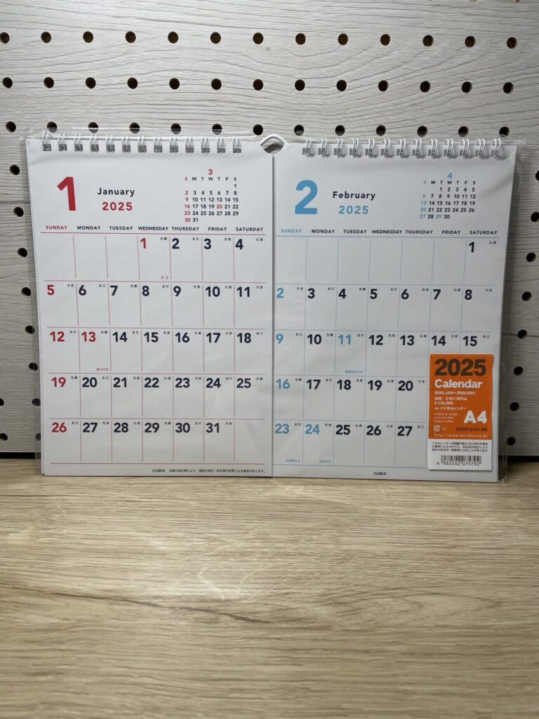 2025年1月と2月が並ぶリング式の2ヶ月カレンダーを背景ボードの前で撮影した写真。