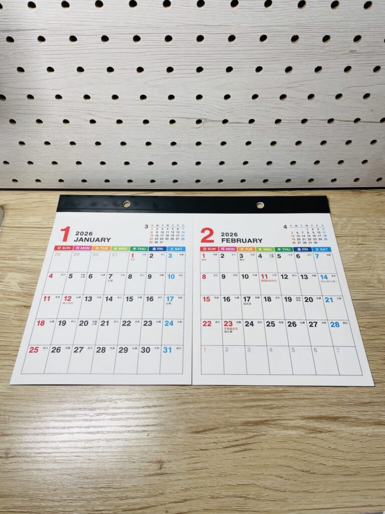 2026年1月と2月が並んだ2ヶ月カレンダーを木目の台の上に置いて撮影した写真。
