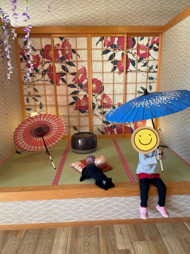 館内フォトスポットの和傘と畳スペース。背景には椿柄の障子が並んでいる。