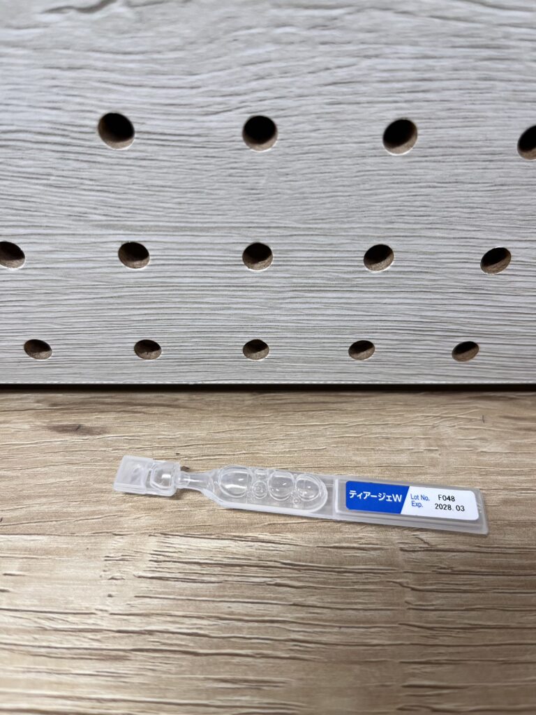 透明容器に入った使い切りタイプの目薬を木目の上に置いた写真。
