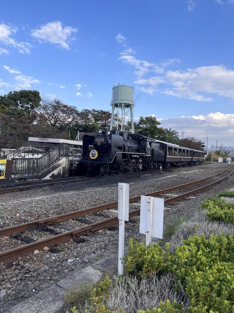 屋外の線路に停車しているSL機関車と給水塔が見える風景。