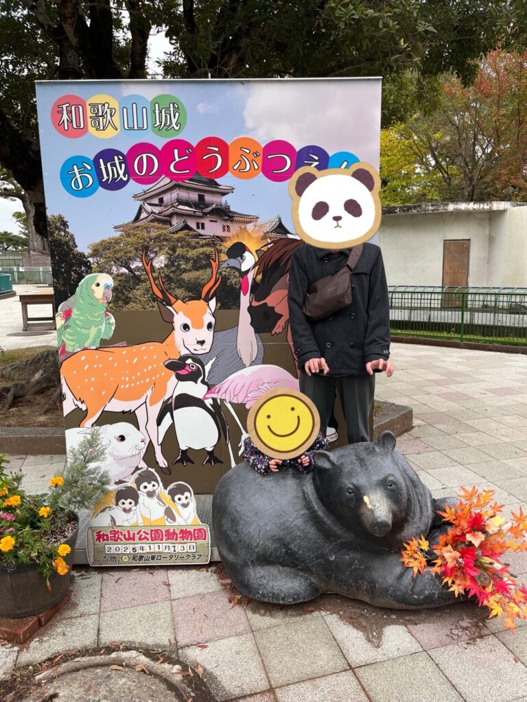 和歌山城公園動物園の看板とクマの像の前で家族が記念撮影している様子