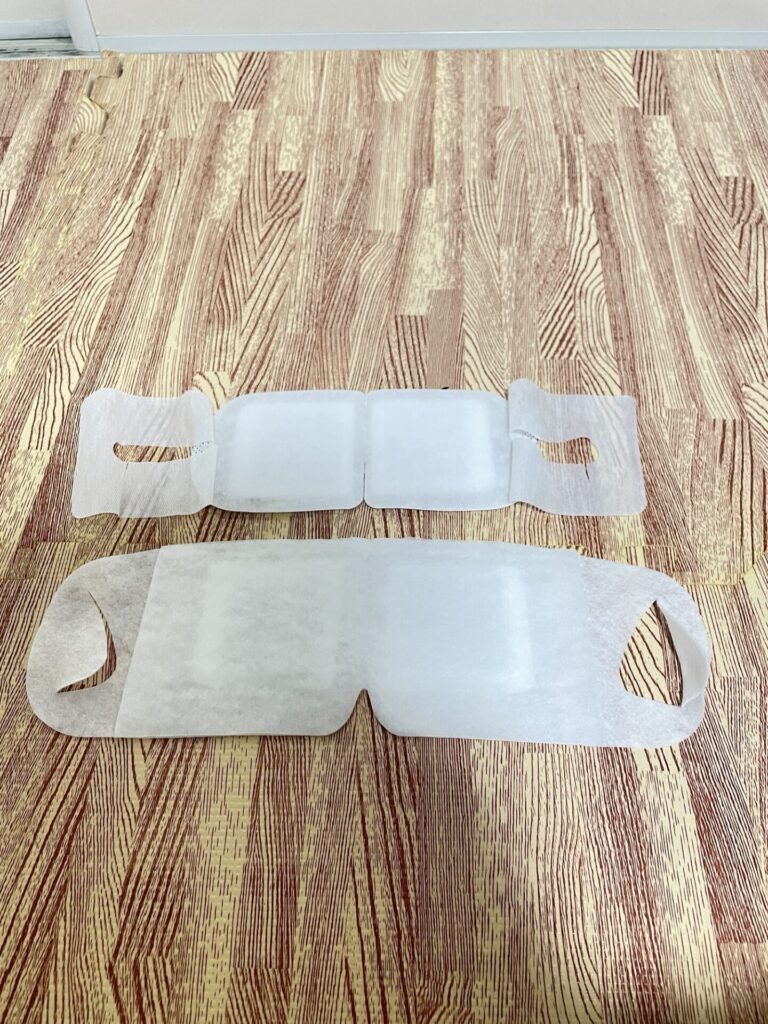 通常サイズと大きめサイズのめぐリズムのアイマスク本体を床の上に並べて大きさを比較している写真。