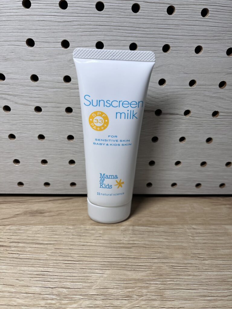 ママ&キッズのサンスクリーンミルクが木目の有孔ボードの前に置かれている。
