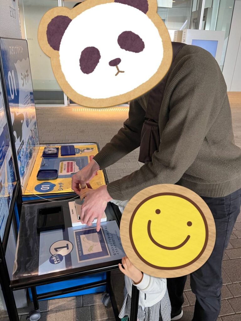 須磨シーワールドのスタンプラリーステーションで、台の上にスタンプ台紙を置いて押している親子。
